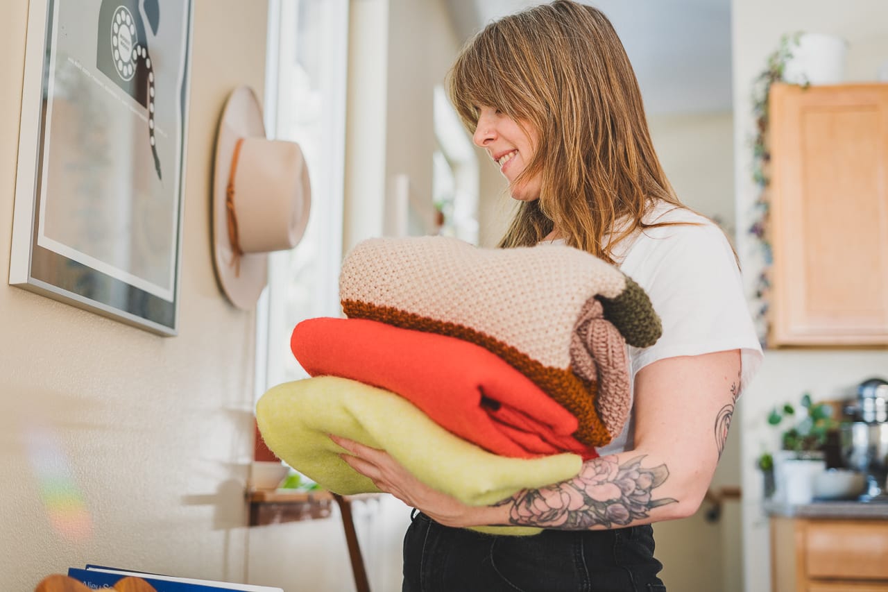 Woman Holding a Pile of Colorful Sweaters by Conscious by Chloé