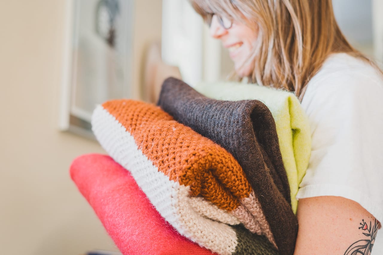 Woman Holding a Pile of Colorful Sweaters by Conscious by Chloé