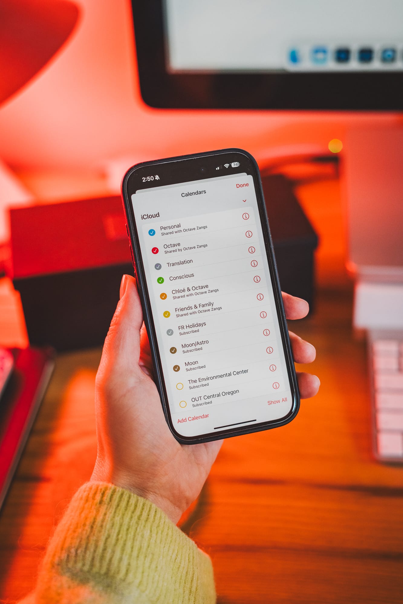 Image of a hand holding an iPhone with Apple Calendar, various calendars are displayed