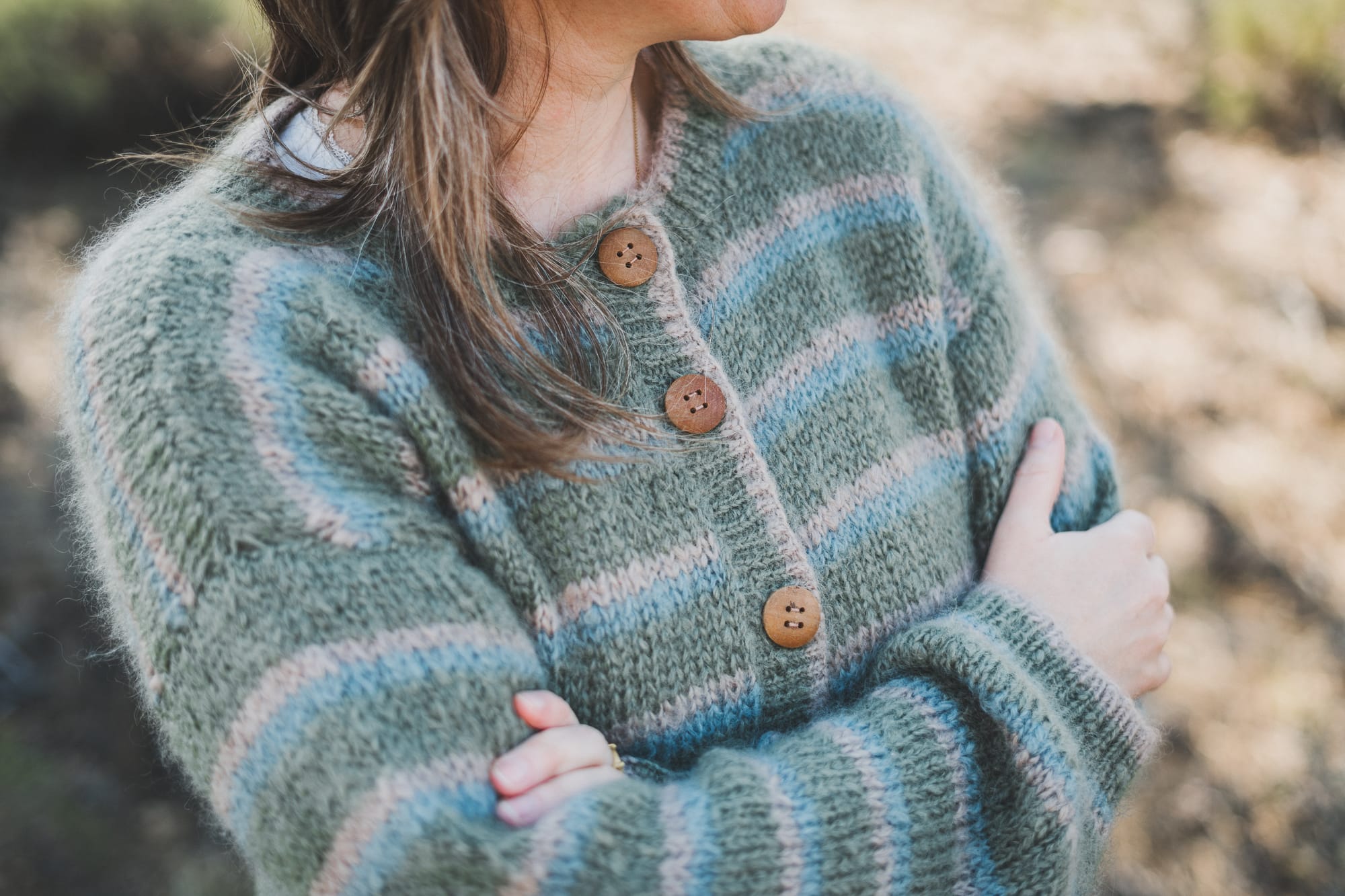 Wooden button details of the Wool and the Gang Piece of Me Cardigan in colors latte green and blue